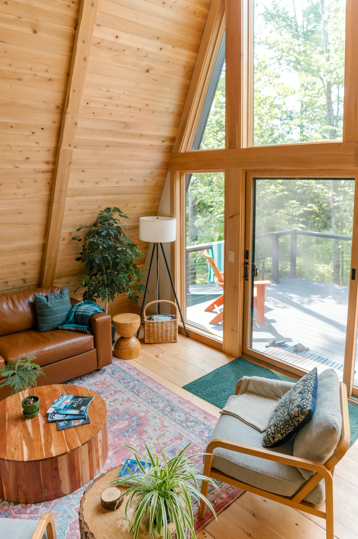 Cozy A-frame cabin living room with a leather sofa, plants and tall windows onto the forest