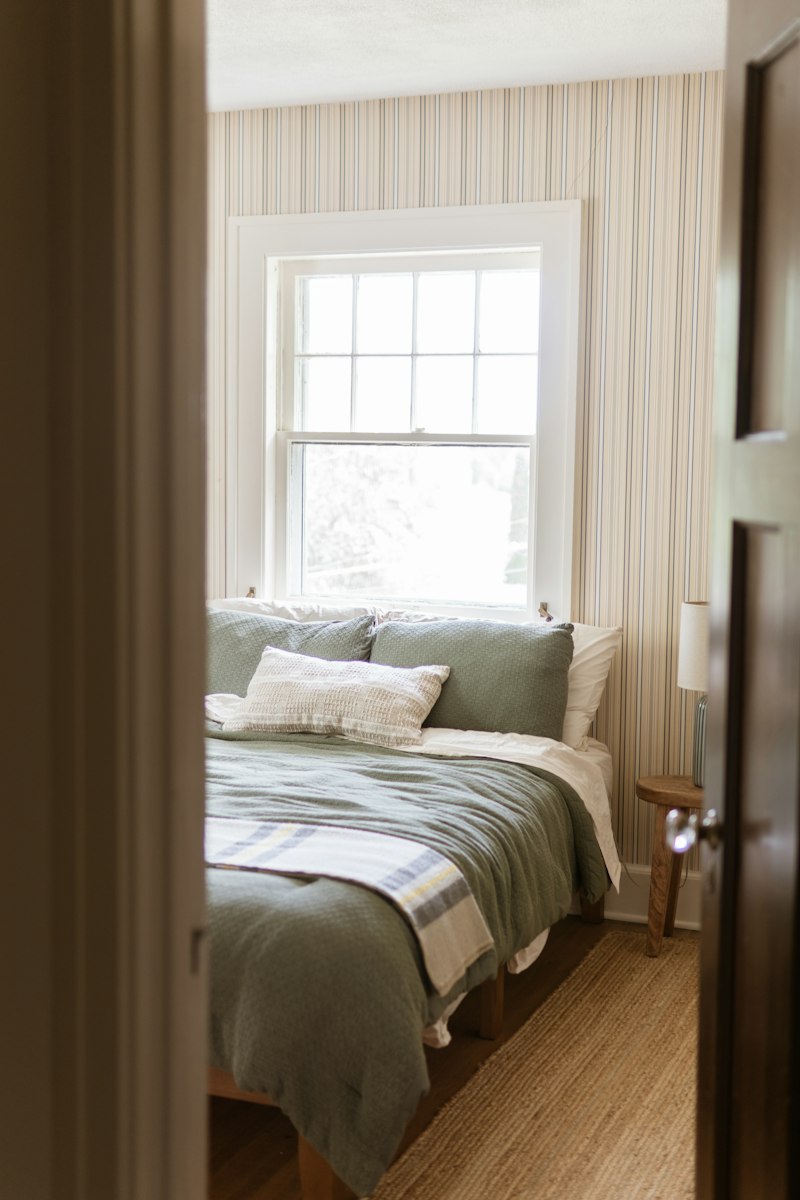 Cozy guest bedroom with a made bed, striped wallpaper and a bright window